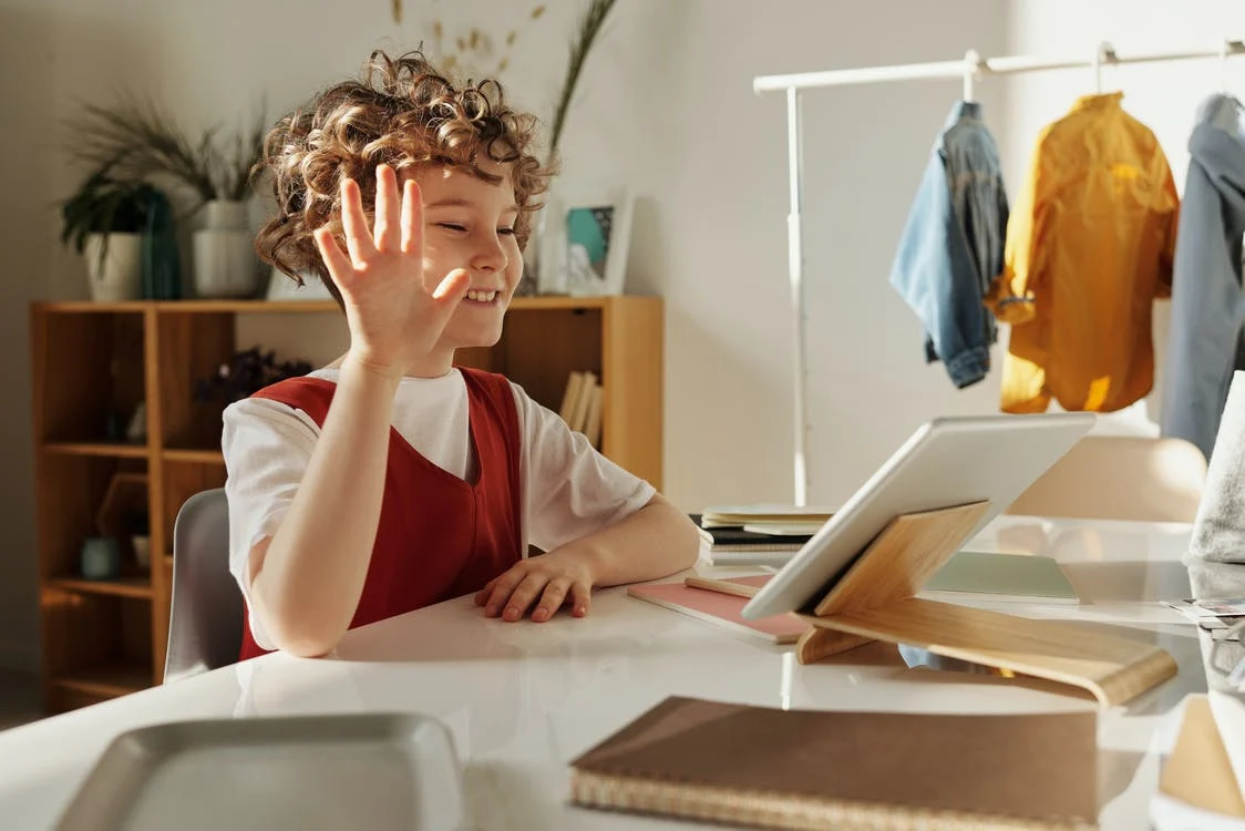 a child raising their hand while looking at the tablet