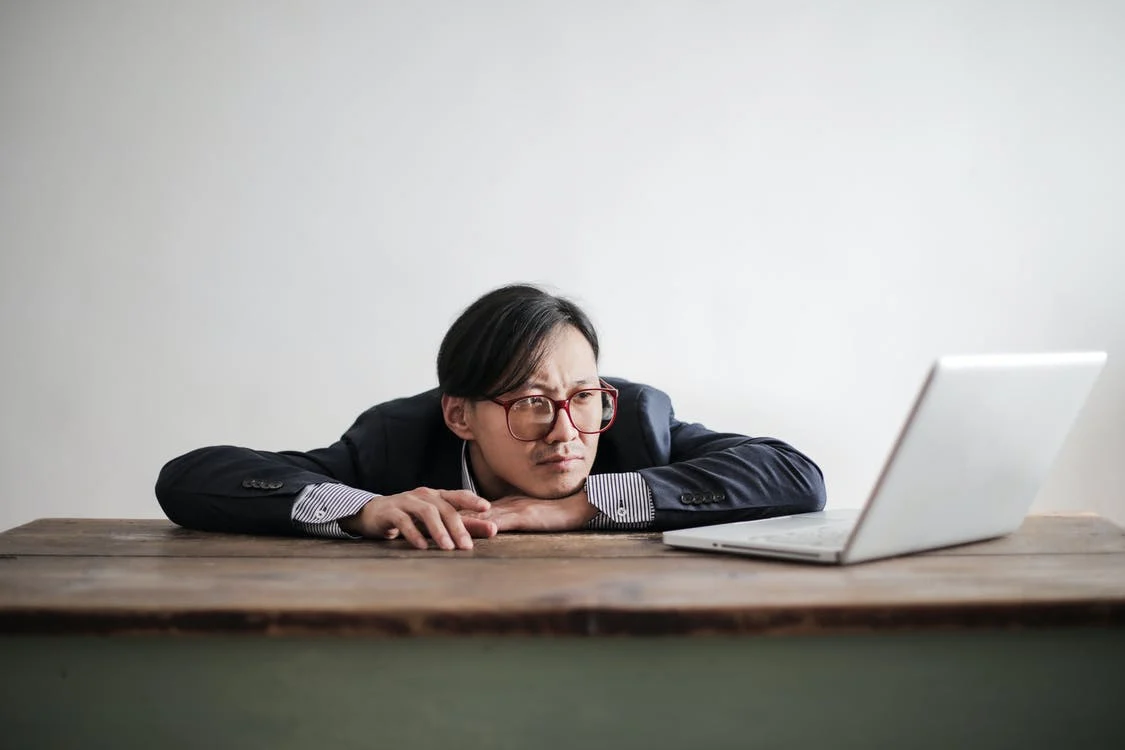 a man with his chin on his hand on the table looking at his laptop