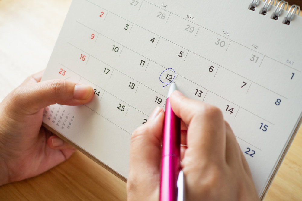 Calendar page with female hand holding pen on desk table