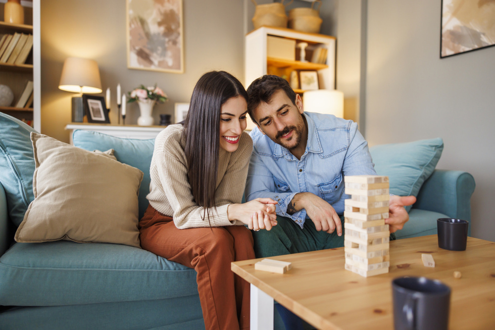 Beautiful young couple in love having fun playing block stacking balance game while relaxing and enjoying spending leisure time together at home