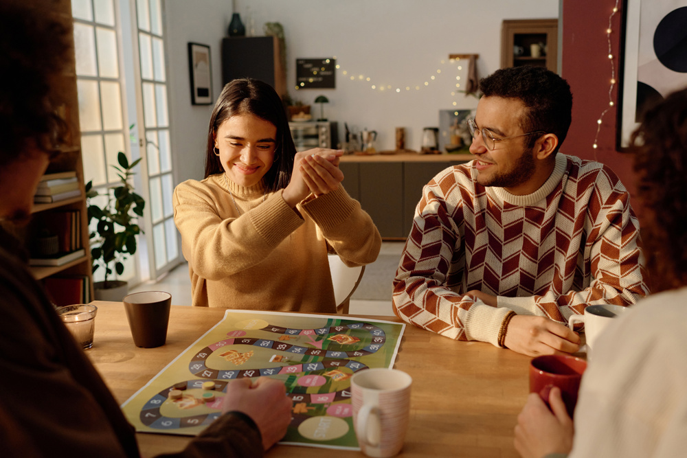 Group of friends looking at young adult woman who smiling while shaking dice, they playing board game at home