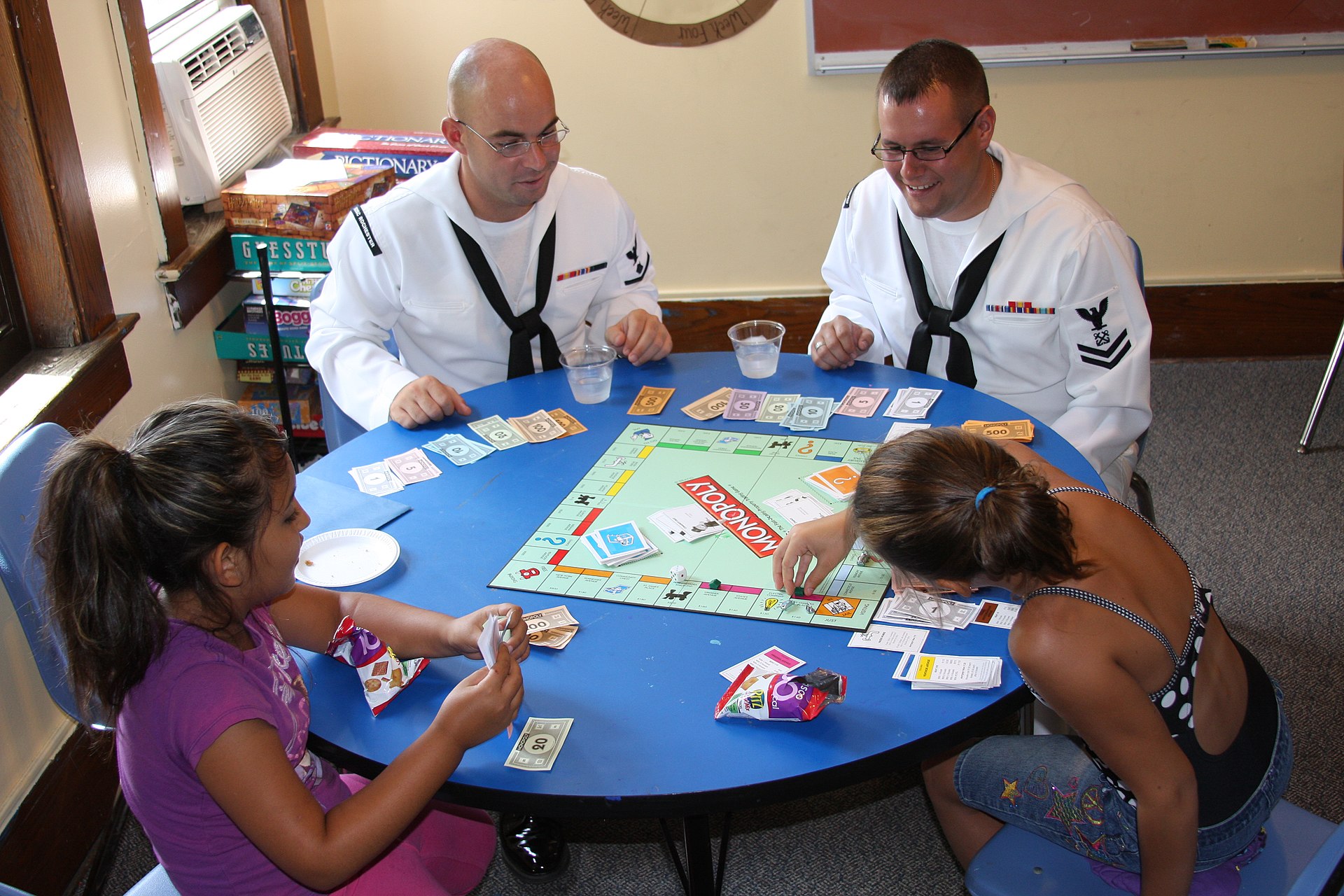 2 men and 2 girls playing Monopoly board game