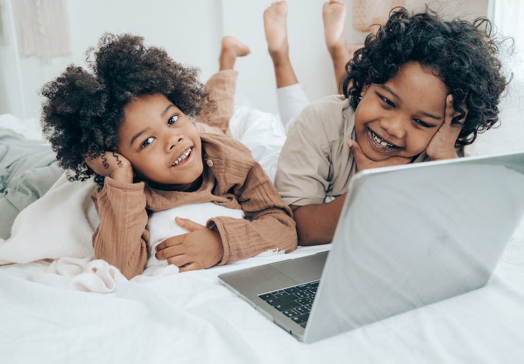 two kids on the bed smiling and looking at the laptop